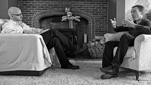 John yorke discussing into the woods to a reviewer infront of a fireplace